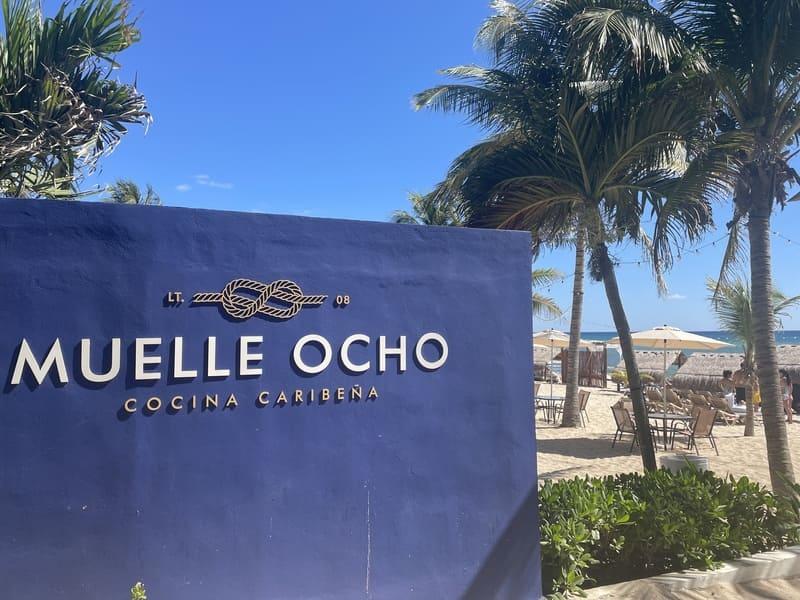 Beachside dining at Muelle Ocho with a clear sky and palm trees.